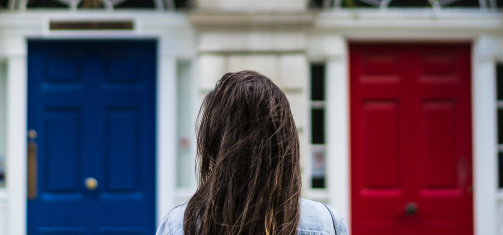 Woman stood infront of two doors, red and blue. Representing choice.